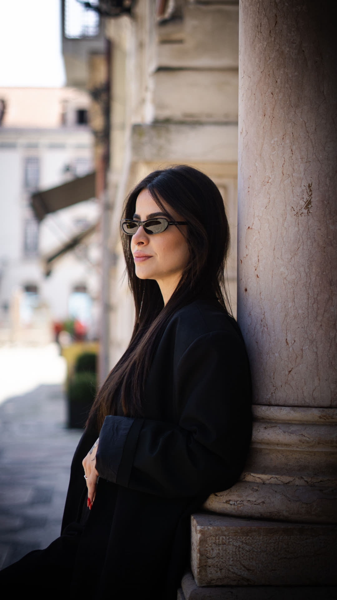 Ragazza con occhiali da sole appoggiata a una colonna di un palazzo storico