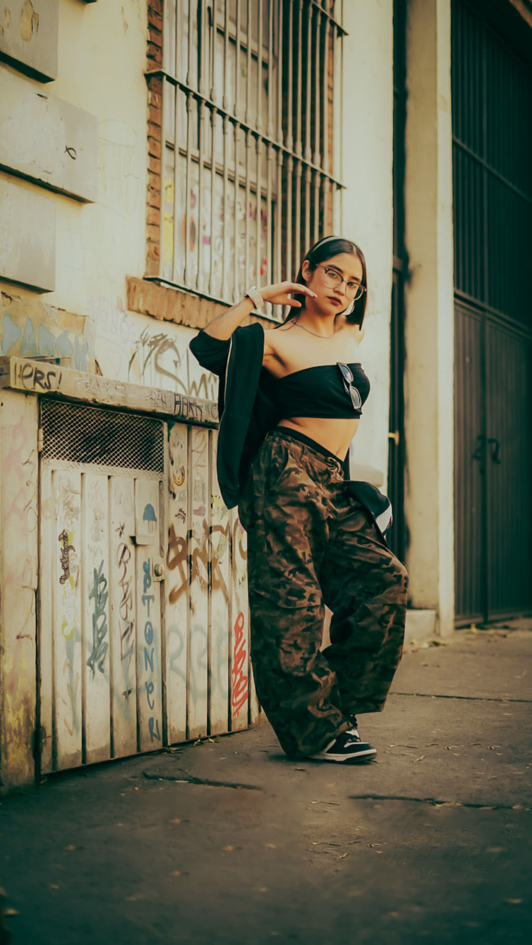 Servizio moda urbano: ragazza con pantaloni cargo appoggiata a una saracinesca con graffiti