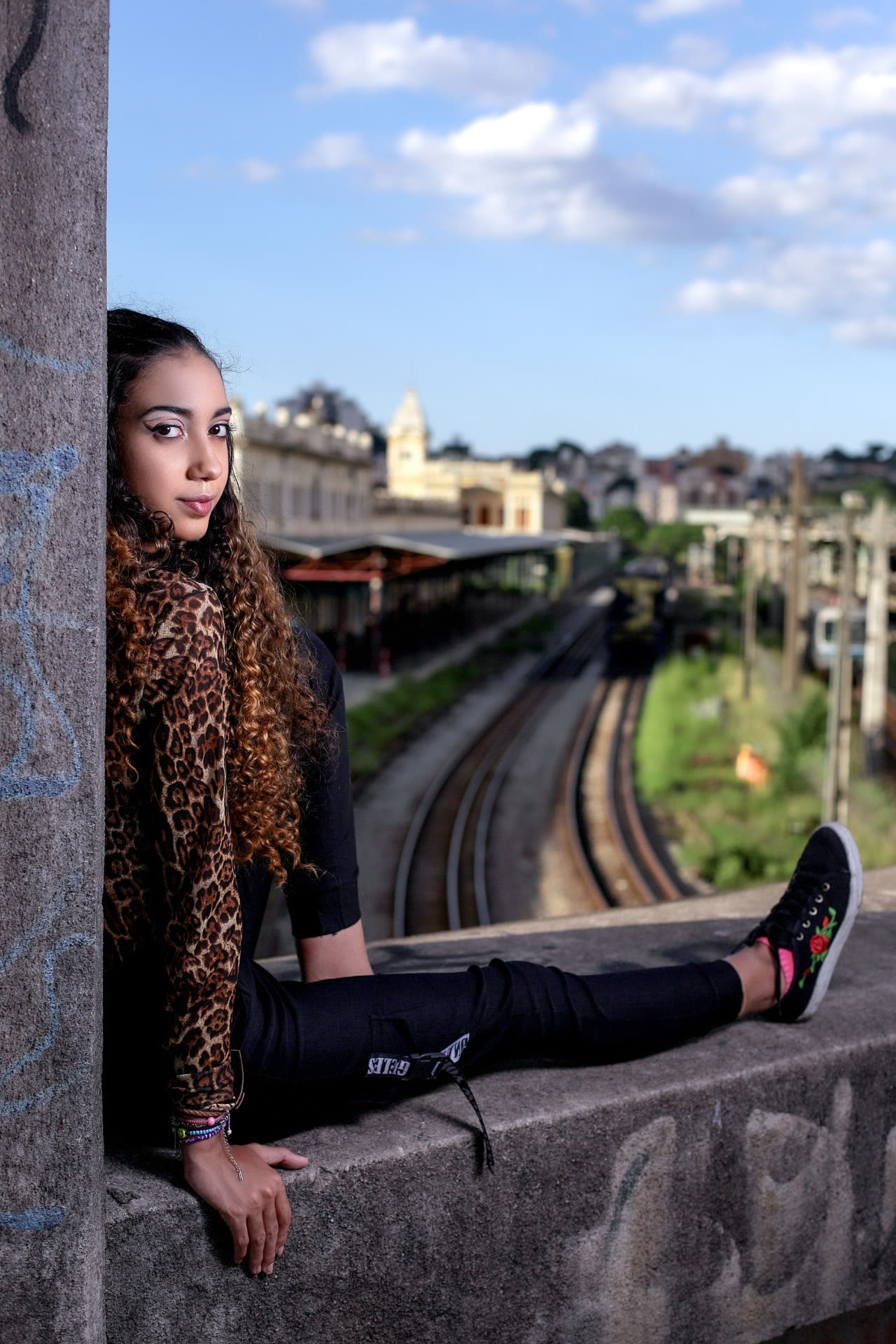 Ragazza con giacca leopardata seduta su un muretto sopra i binari della ferrovia