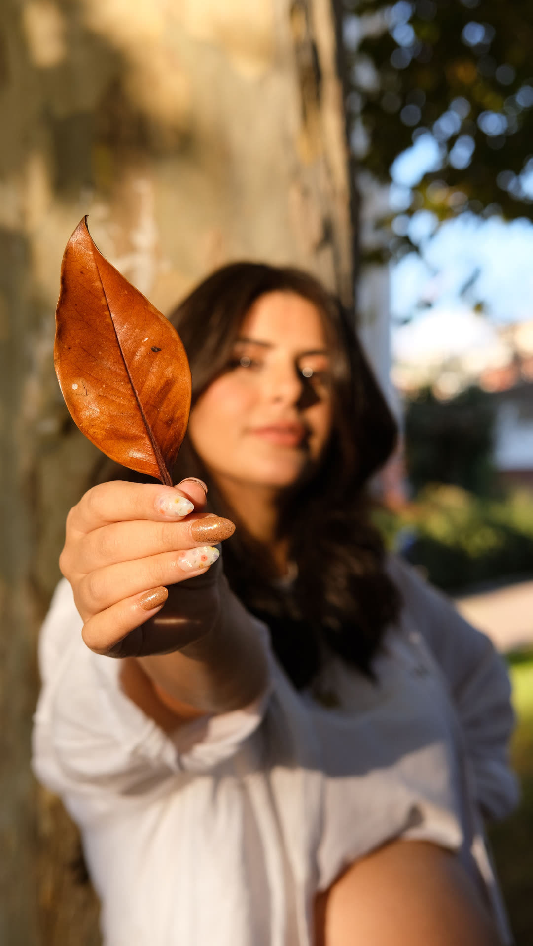 Ritratto all'aperto di ragazza che porge una foglia autunnale verso l'obiettivo